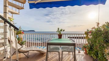 Un balcon avec une table et des chaises, donnant sur une plage et la mer.