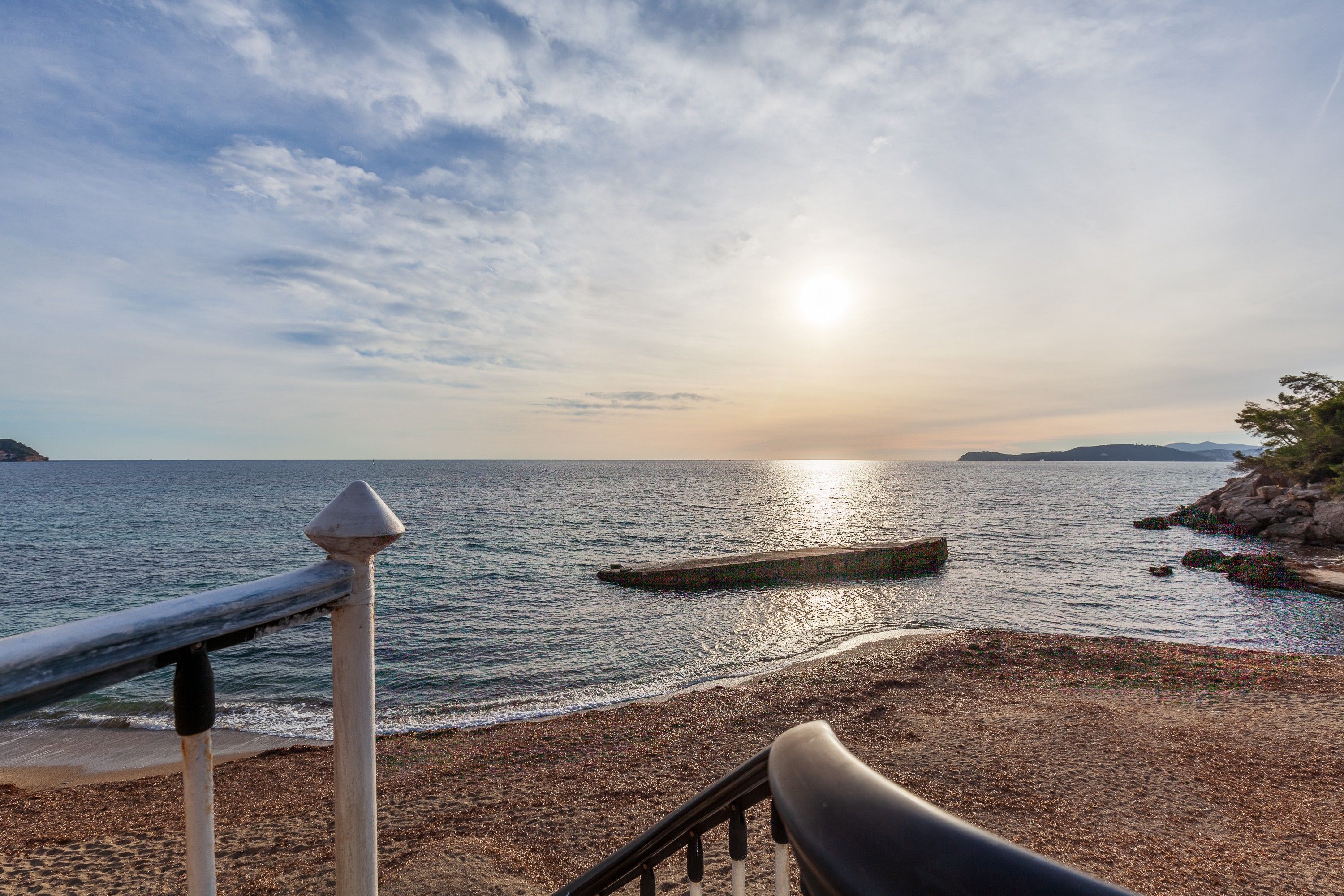 A coastal scene with a pebbly beach, a wooden pier, and a clear sky.