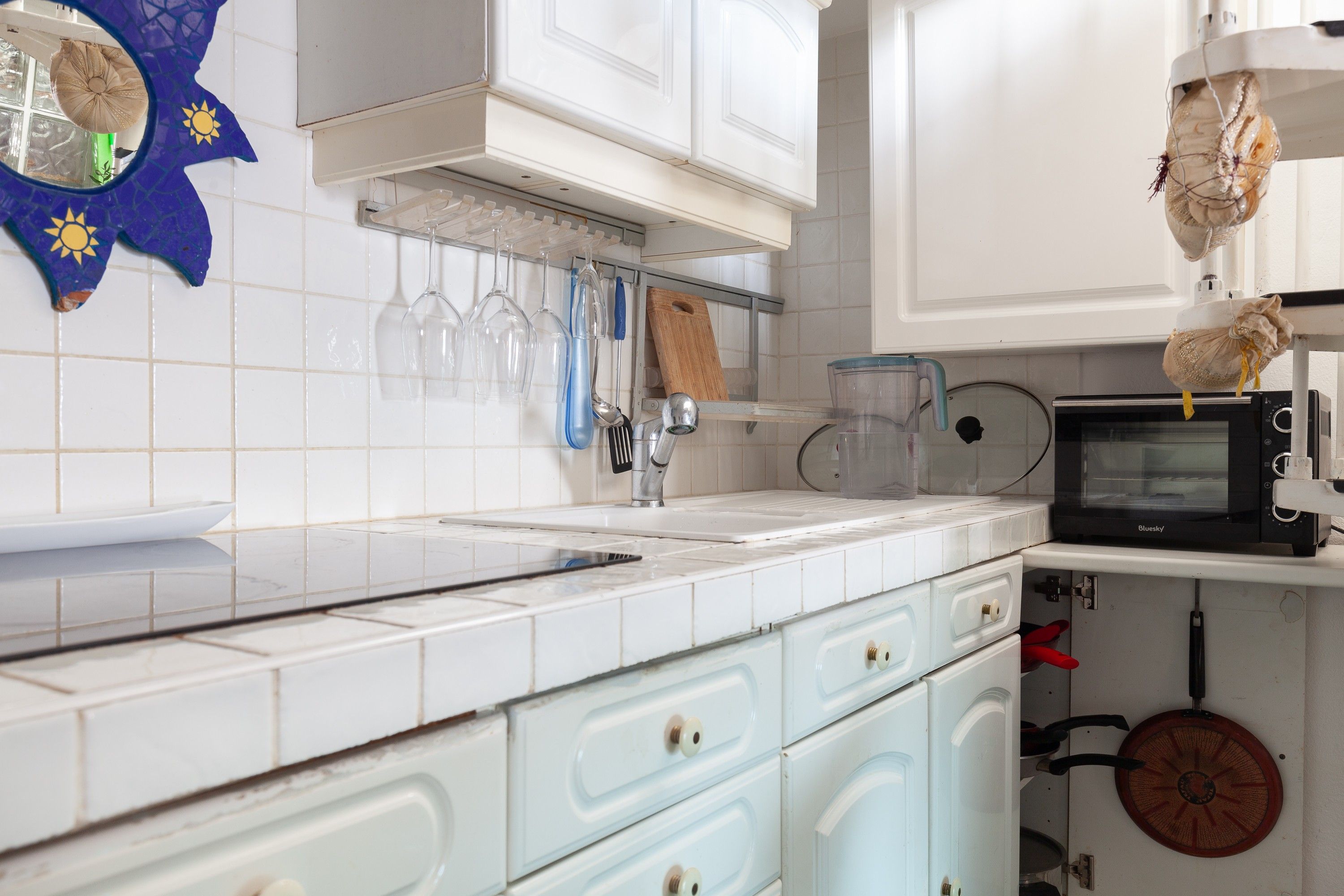 Een keuken met witte kastjes, een magnetron en diverse keukengerei.