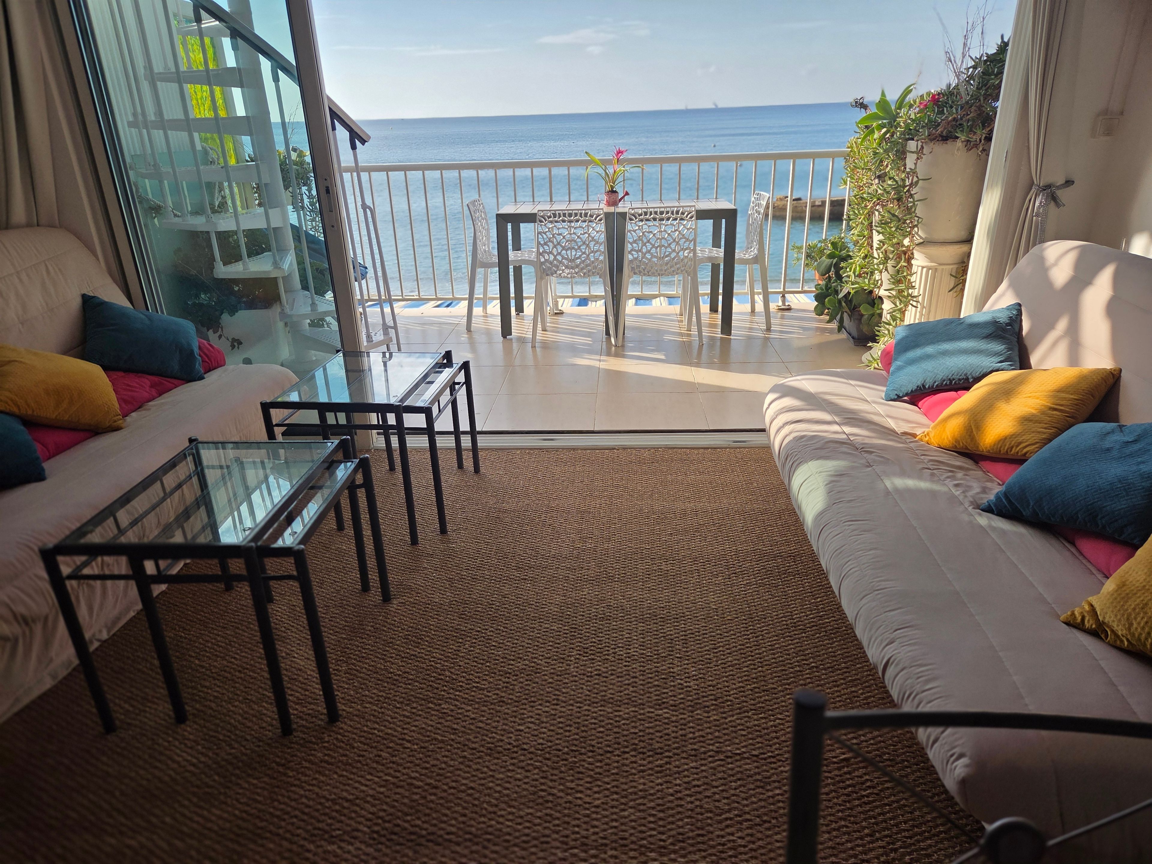 A balcony with a view of the sea, furnished with a sofa, chairs, and a table.