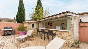 Un patio con sillones de descanso, una parrilla y un muro de piedra con zona de bar.