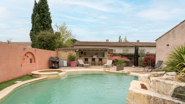 Una piscina con borde de piedra, sillas de descanso y zona de barbacoa.