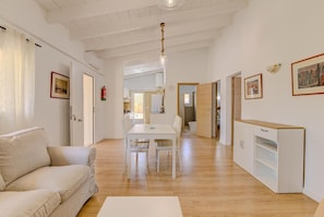 A spacious living area with a white sofa, a dining table, and a kitchenette.