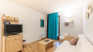 Ein modernes Wohnzimmer mit Fernseher, Sofa, Couchtisch und einer kleinen Bücherablage.