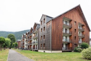 Une rangée d’immeubles d’appartements modernes en bois, dotés de balcons, un sentier de gravier et un paysage montagneux en arrière-plan.