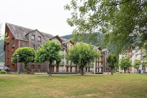 Un immeuble à plusieurs étages doté de balcons, entouré d’arbres et d’une zone herbeuse.