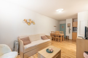Un espace de vie compact comprenant un canapé, une table à manger et des chaises, un petit coin cuisine et un radiateur.