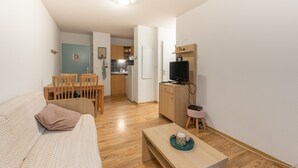 Ein Wohnzimmer mit einer Couch, einem Couchtisch, einem Fernseher und einer Küche im Hintergrund.