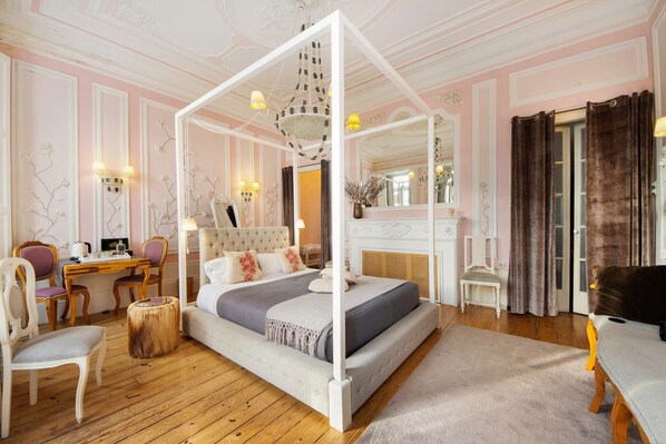 Ein Bett mit Baldachin, ein Schreibtisch mit Stuhl, ein runder Tisch und ein Stuhl in einem Zimmer mit rosa Wänden und Holzboden.