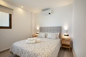 Une chambre à coucher comprenant un lit, deux tables de chevet, un appareil de climatisation et une fenêtre avec un store.
