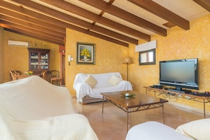 A living room with a sofa, a coffee table, a TV, and a wooden ceiling.