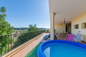 Un balcón con vistas a un paisaje verde, una piscina inflable azul y una mesa con sillas.
