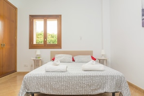 Un dormitorio con cama, dos mesitas de noche, una ventana y una puerta.