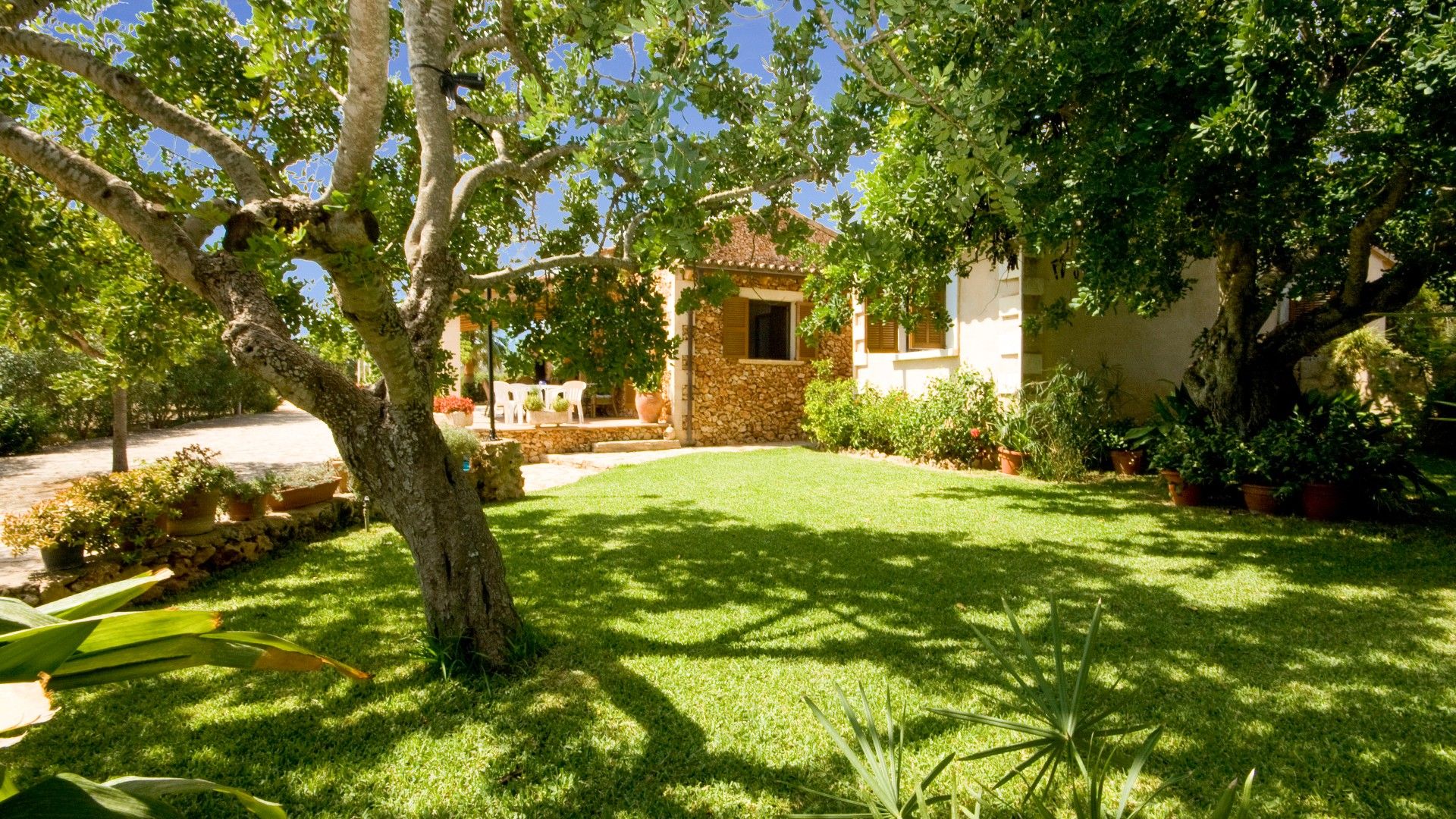 A well-maintained garden with a stone building, a lawn, and various potted plants.