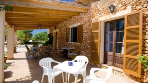 Un patio al aire libre con paredes de piedra, contraventanas de madera y mobiliario de plástico blanco.