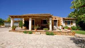 A stone house with a covered patio, outdoor seating, and potted plants.