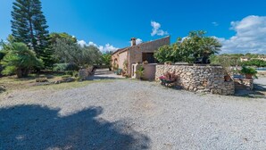 A stone building with a gravel driveway, surrounded by trees and potted plants. - Villa 'Sa Plana Ref 42' with Mountain View, Private Pool and Wi-Fi (Cala Bona)
