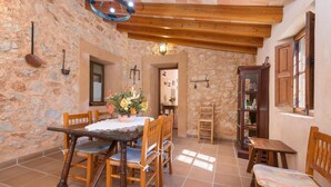 A stone-walled room with a wooden table and chairs, a wooden cabinet, and a tiled floor. - Villa 'Sa Plana Ref 42' with Mountain View, Private Pool and Wi-Fi (Cala Bona)