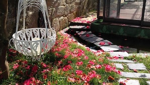 Un jardín con una mecedora blanca, un muro de piedra y un sendero con flores rosadas dispersas.