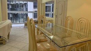 Un comedor con mesa de vidrio y sillas de mimbre, un balcón con vistas, y una puerta decorada con un adorno.
