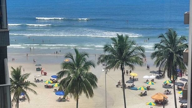 Una playa con palmeras, sombrillas y gente.