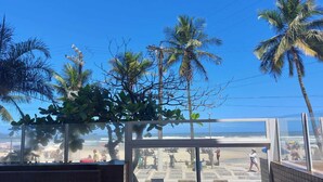 Vista desde un balcón con vista a una playa, palmeras y cielo despejado.