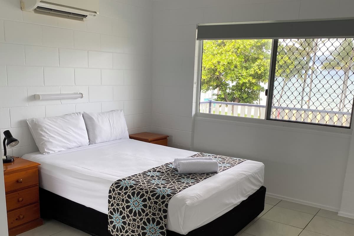 A bedroom with a bed, a nightstand, a bedside table, a window with a view, and a ceiling fan.