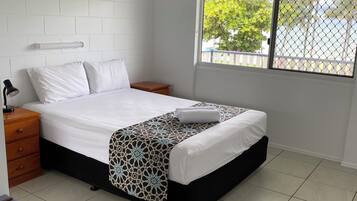 A bedroom with a bed, a nightstand, a bedside table, a window with a view, and a ceiling fan.