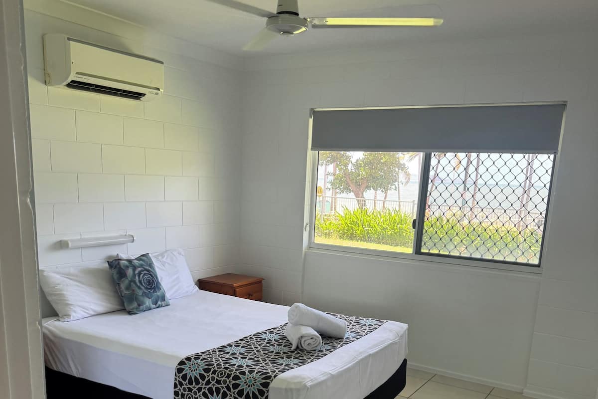 A neatly arranged bedroom with a bed, bedside table, and a window with a view.