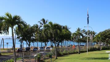 A grassy outdoor area with a white table and chair, palm trees, and a view of the ocean.