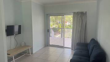 A living room with a flat-screen TV mounted on the wall, a bench, a sofa, and a sliding glass door leading to an outdoor area.