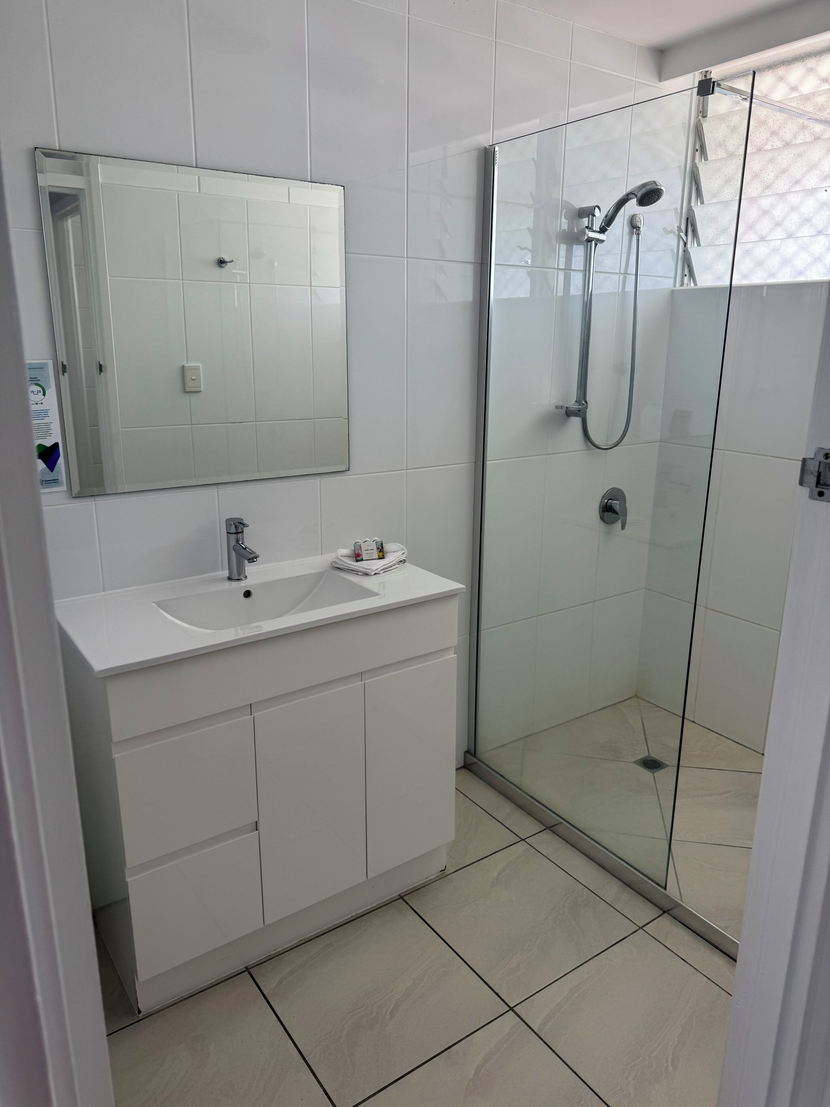 A modern bathroom with a glass shower enclosure, a white sink, and a large mirror.