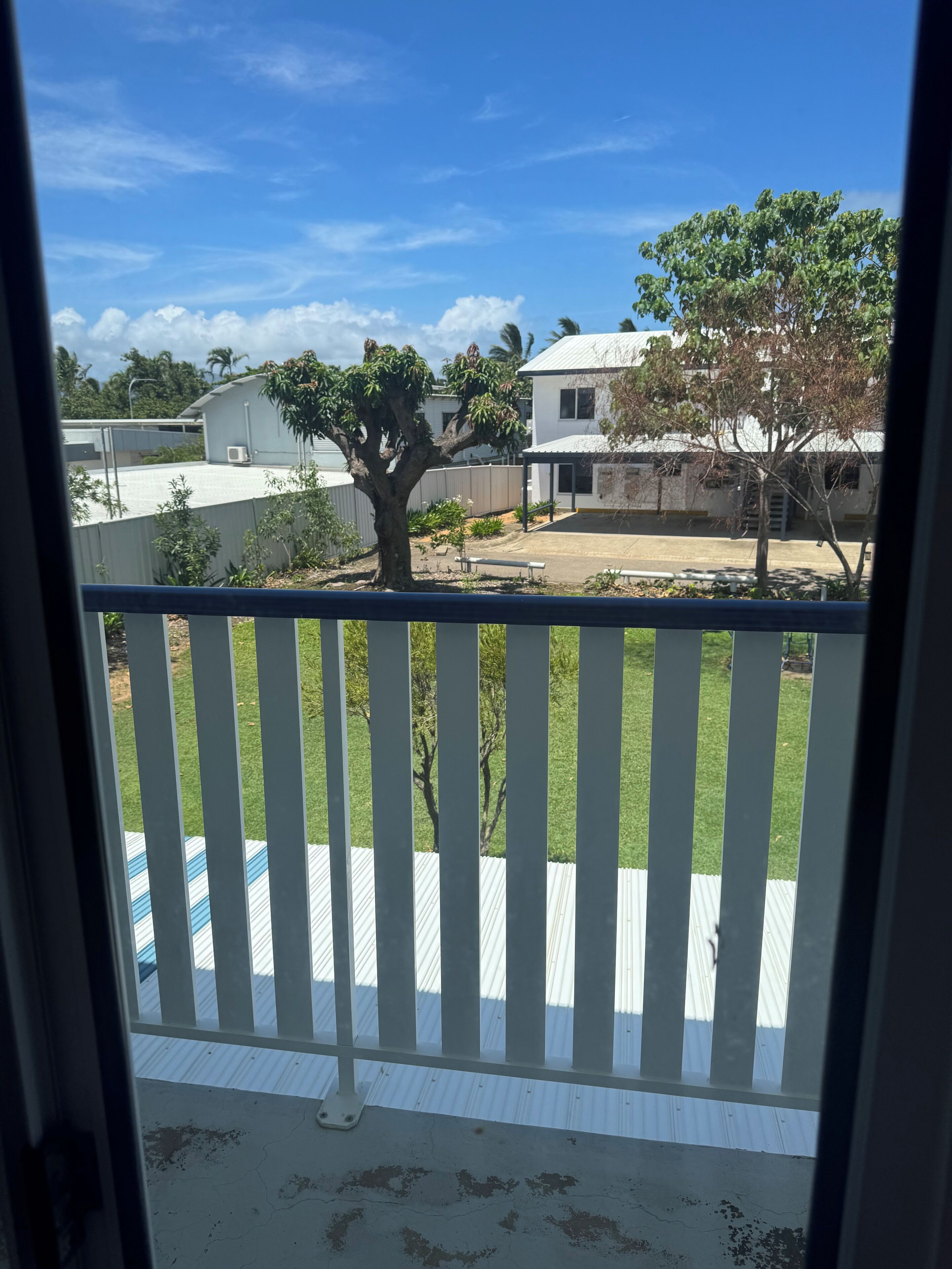Un balcón con vistas a una zona residencial, que incluye un árbol y casas.