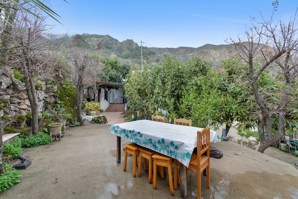 Une terrasse extérieure avec une table et des chaises, entourée d’arbres et d’un mur en pierre.