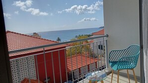 Un balcon avec un toit recouvert de tuiles rouges, une chaise bleue et une vue sur la mer.
