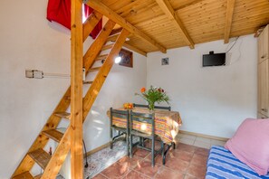 Une pièce avec un escalier en bois, une table recouverte d’une nappe à motifs floraux, un lit avec une couverture à rayures et un téléviseur fixé au mur.