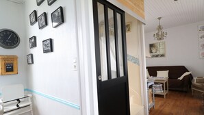 Ein Zimmer mit Holzboden, einer schwarzen Tür, einer weißen Wand mit gerahmten Bildern, einer Uhr und einem kleinen Tisch mit einem Stuhl.