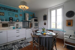 Una cocina con pared azul, armarios blancos, una mesa de comedor con platos y cubiertos, y un reloj en la pared.