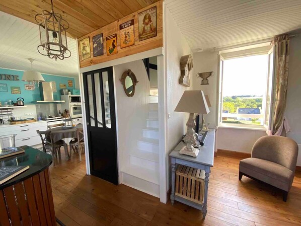 A room with a wooden ceiling, a dining area with a table and chairs, a kitchen with cabinets and appliances, and a window with a view.