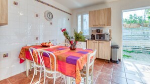 Een keuken met witte tegels, een eettafel met stoelen, een klok en een raam.