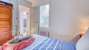 Een slaapkamer met een bed, een houten garderobe, een raam en een deur die uitkomt op een buitengebied.