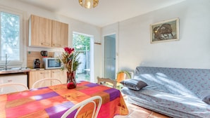 Een compact woongedeelte met een kitchenette, een eethoek met tafel en stoelen, een bank en een schilderij aan de muur.