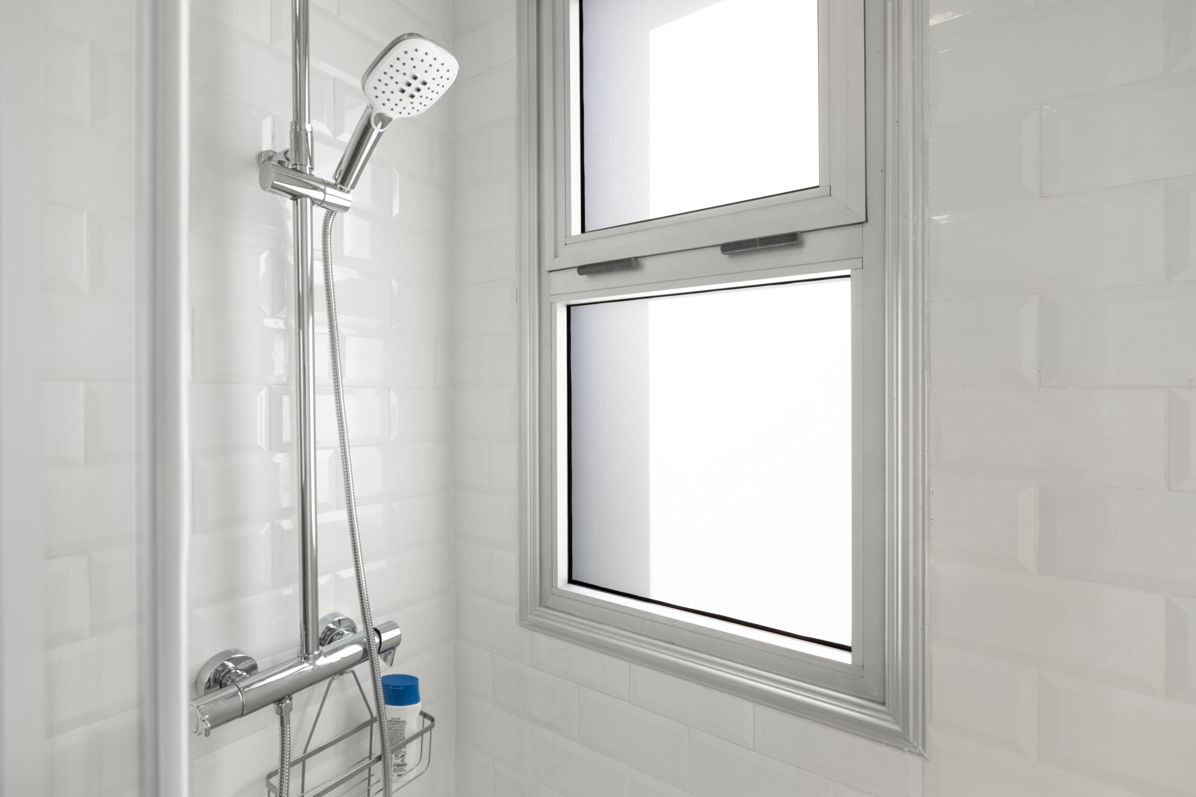 Une douche équipée d’un pommeau de douche à main, d’un panneau de commande fixé au mur et d’une fenêtre située au-dessus de la douche.