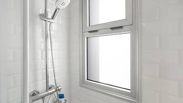 Une douche équipée d’un pommeau de douche à main, d’un panneau de commande fixé au mur et d’une fenêtre située au-dessus de la douche.