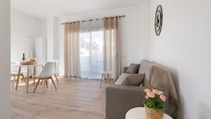 Una sala de estar moderna con un sofá, una pequeña mesa redonda con una planta, un comedor con sillas y vistas a través de un amplio ventanal.