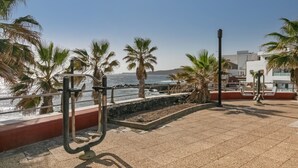 Paseo marítimo con una estación de ejercicios, palmeras y vista al océano.