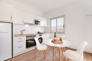 A modern kitchen with white cabinets, a built-in oven, a microwave, and a dining area with a white table and chairs.
