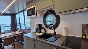 A modern kitchen with a built-in microwave, a round window above the sink, and a dining area with a view of the sea.