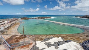 Eine Küstenbadebucht mit klarem Wasser, Felsformationen und einer Aussichtsplattform.