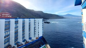 Ein Hotel an der Küste mit mehreren Etagen, Balkonen und Blick auf das Meer und ferne Berge.